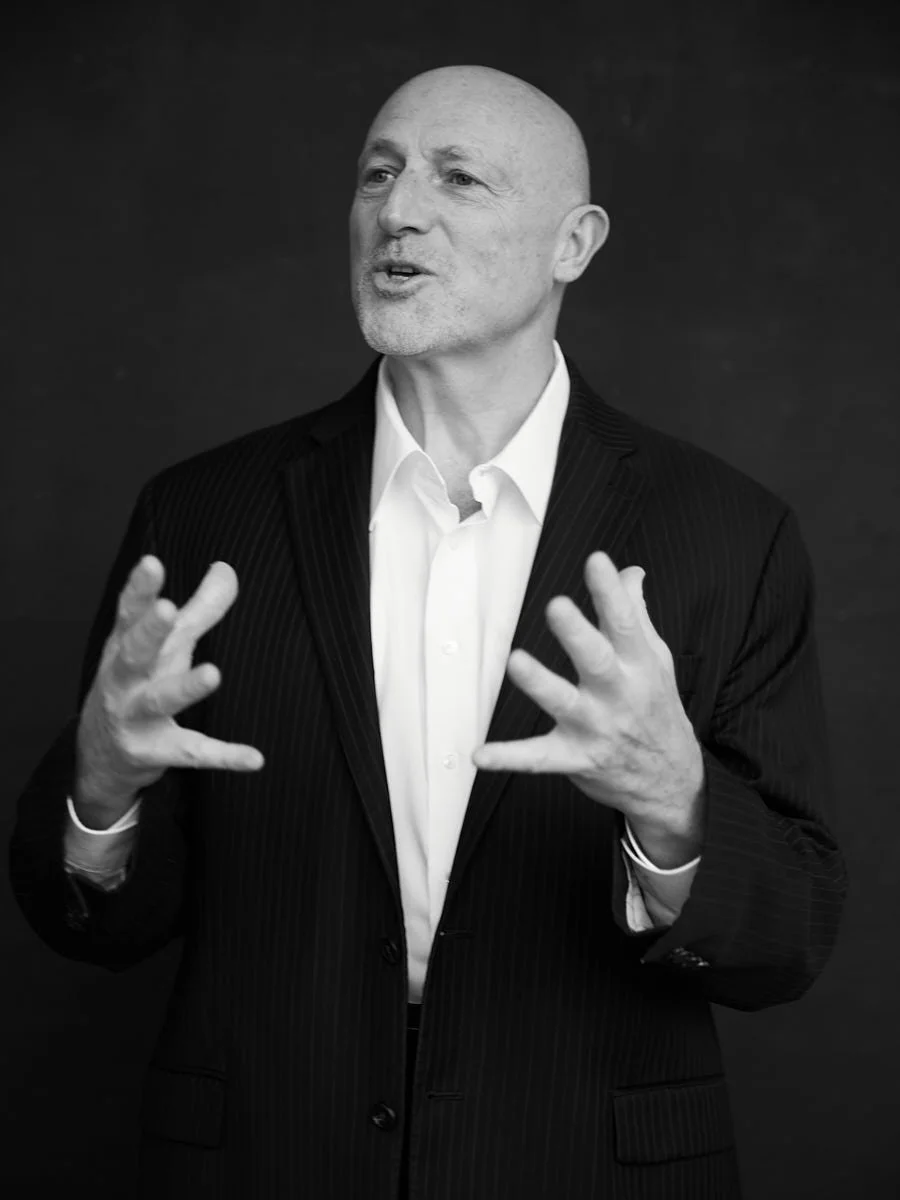 Black-and-white portrait of a bald man gesturing while speaking.