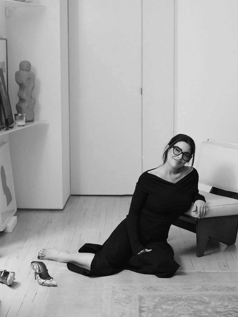 Black-and-white photograph of a woman seated on the floor beside a sofa.