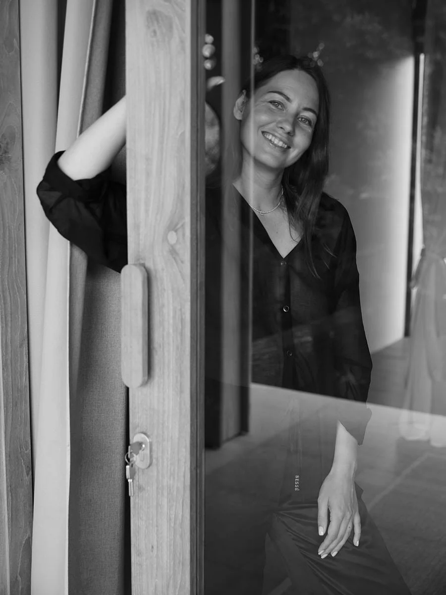 Black-and-white portrait of a smiling woman beside a doorframe.