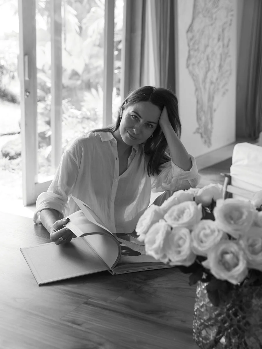 Black-and-white photograph of a woman reading at a table beside flowers.