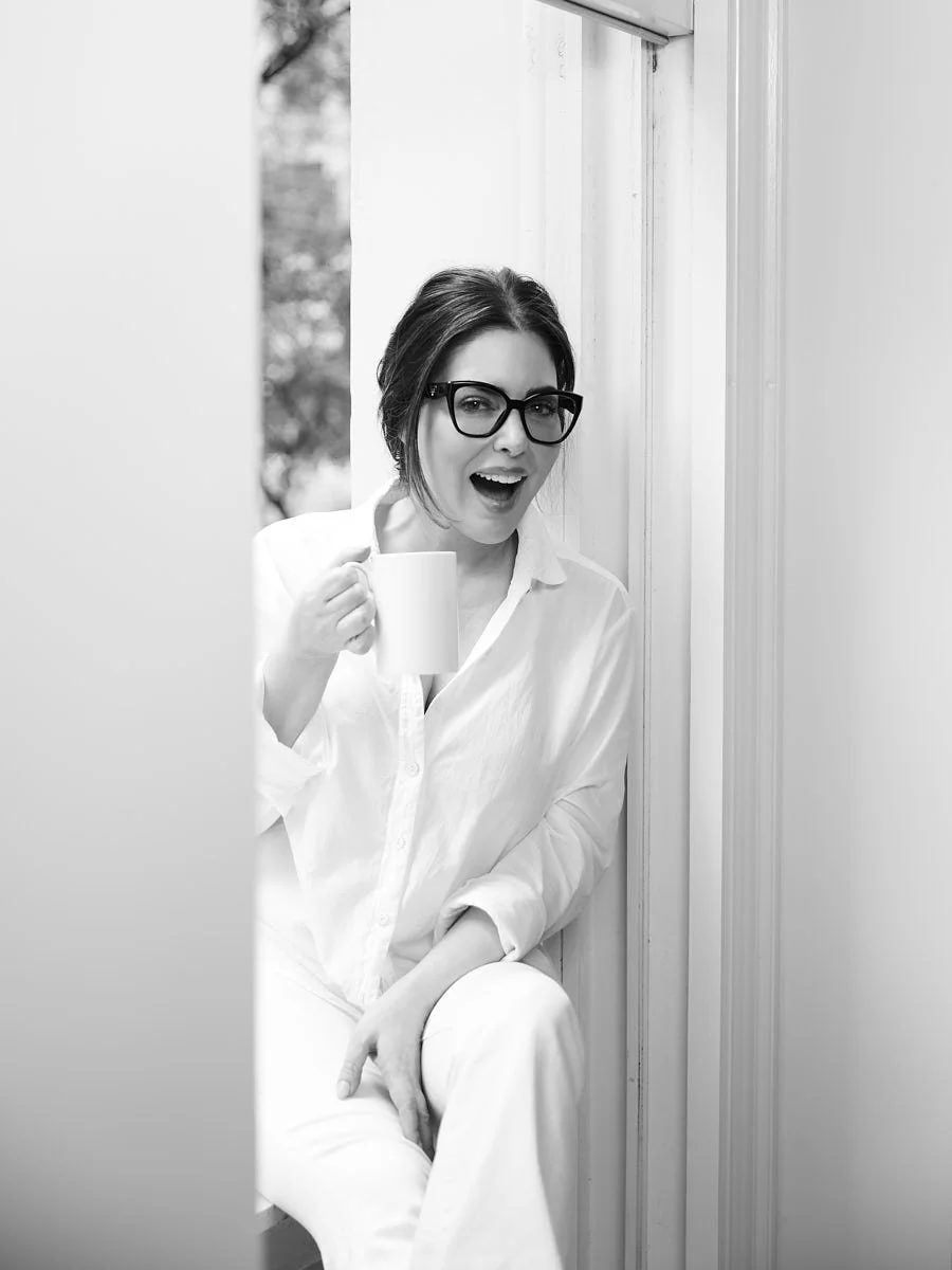 Black-and-white seated portrait of a woman in white clothing and glasses.