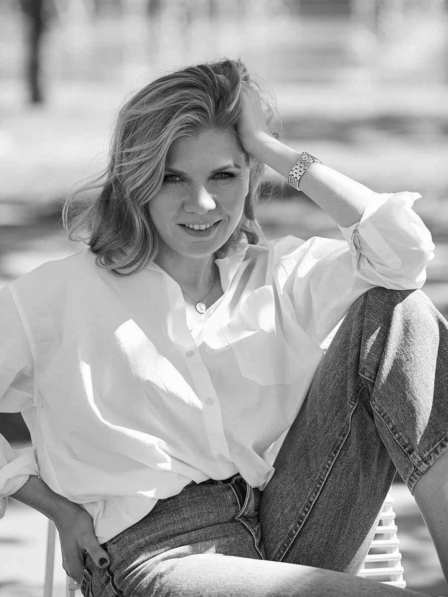 Woman in a white shirt seated outdoors in a black-and-white portrait.