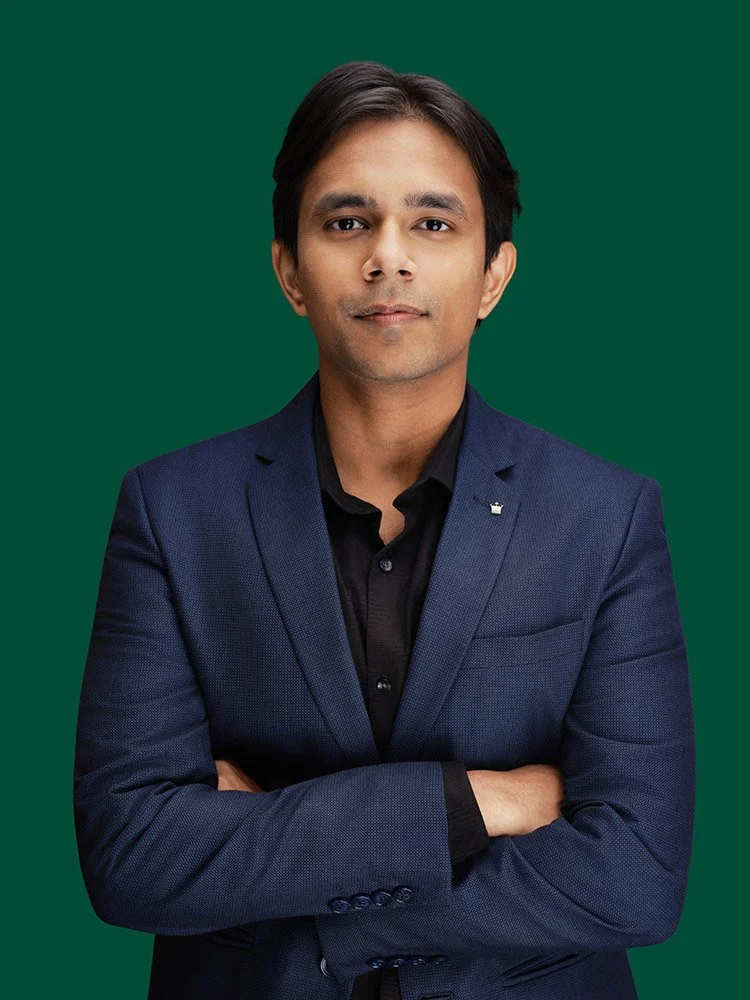 Person in a blue suit standing with arms folded against a green background.