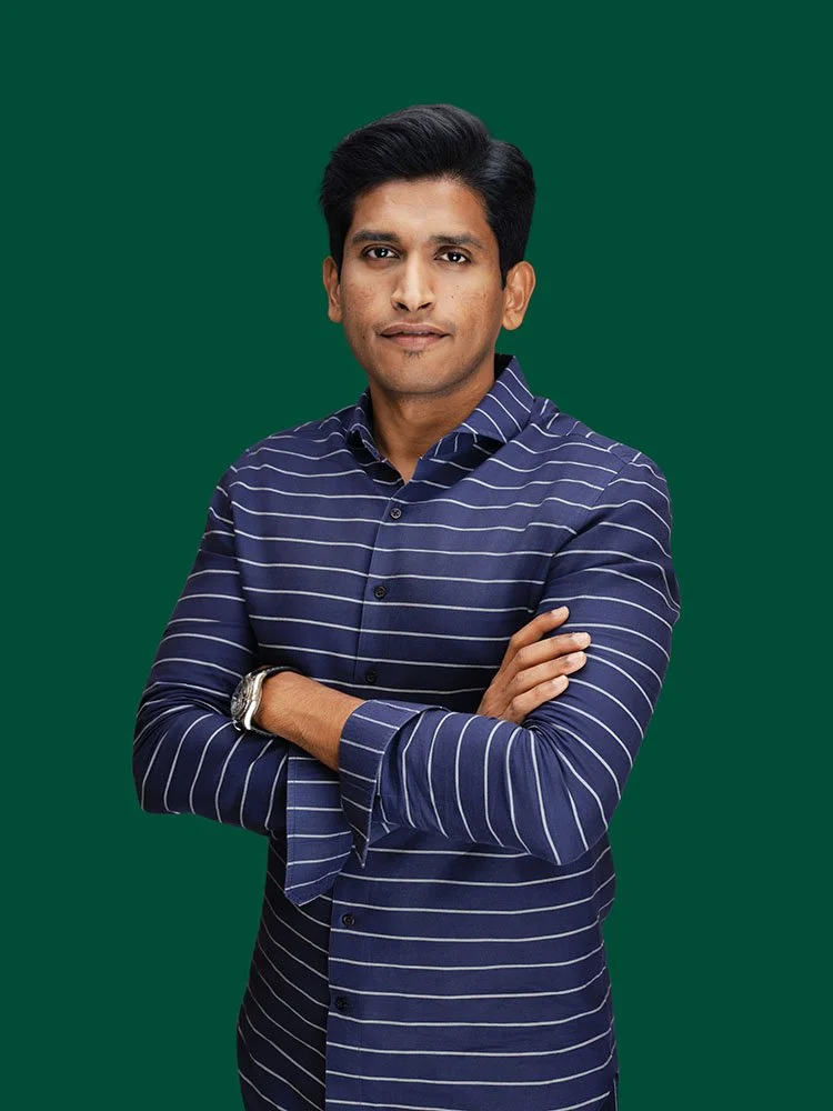 Person in a striped shirt standing with arms folded against a green background.