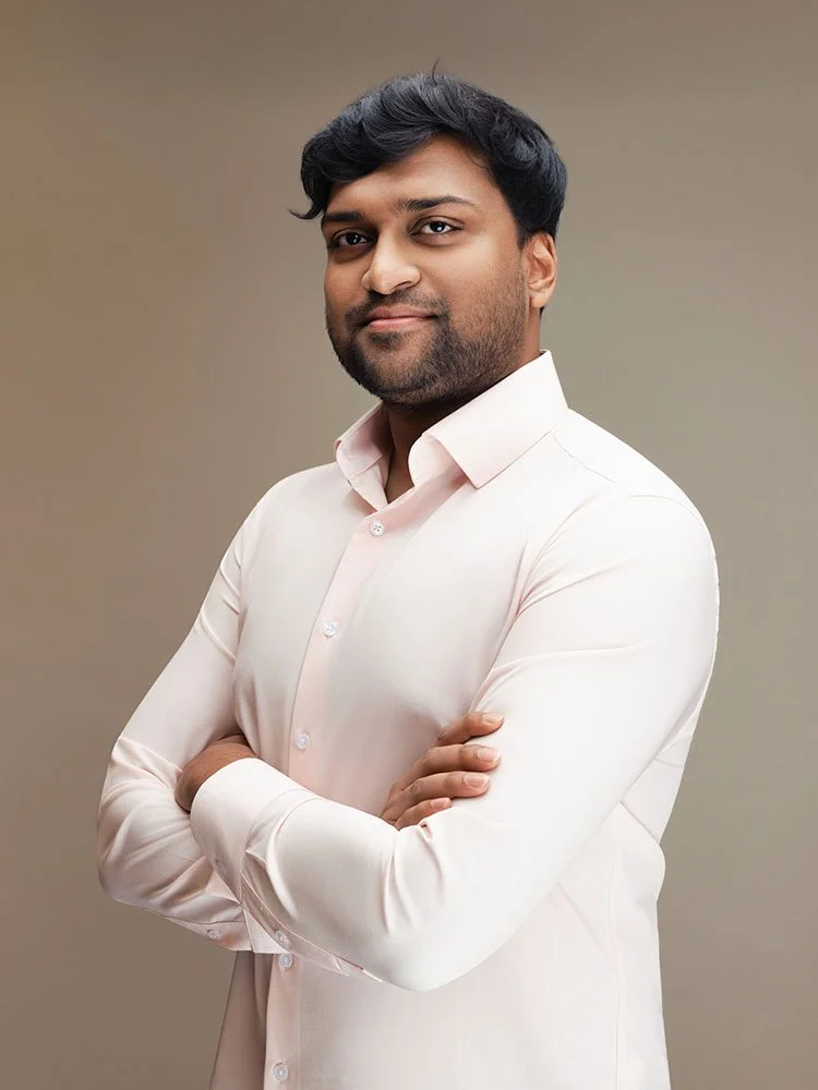 Person in a white shirt with arms folded against a light neutral background.