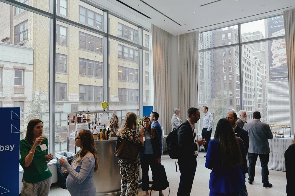 Guests talking in a bright reception room with tall windows.