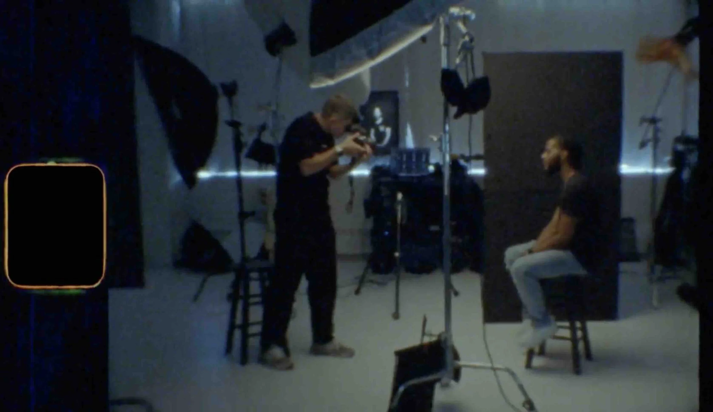 Photographer and seated subject during a portrait session, shown on a studio monitor.