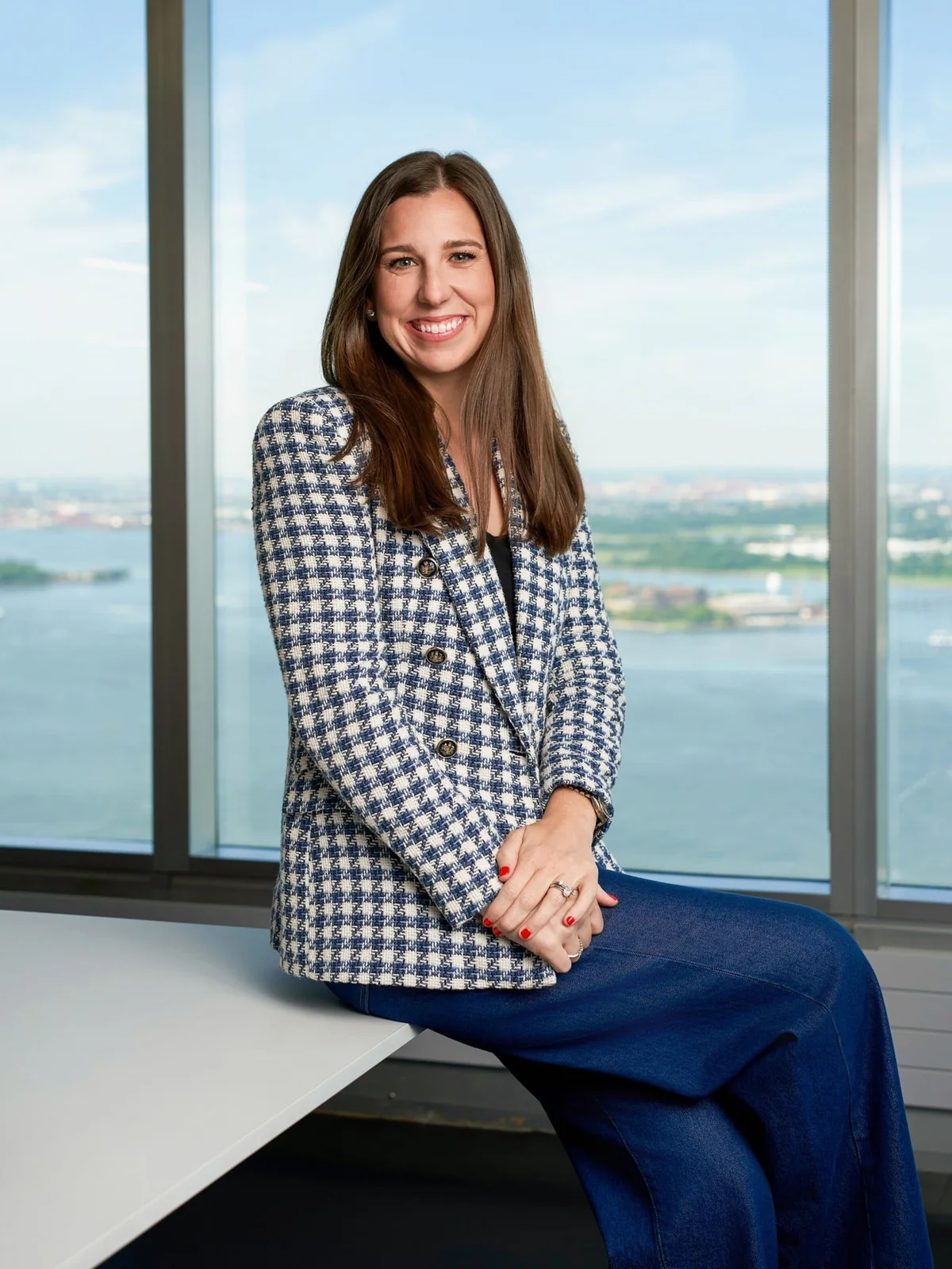 An Onshore leadership portrait: a woman in a checked jacket seated beside large office windows.