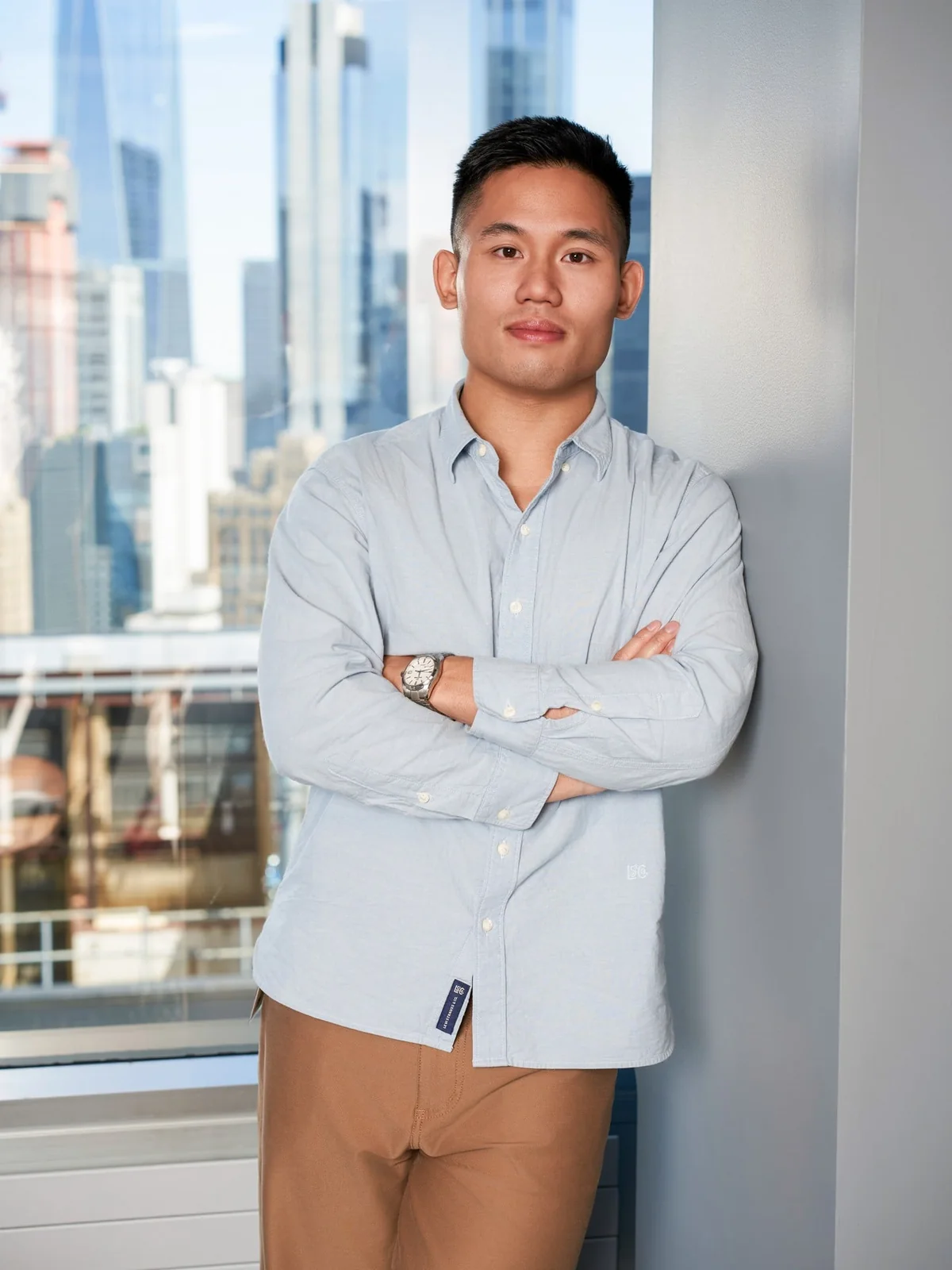 Portrait of a person in a light blue shirt standing beside office windows.