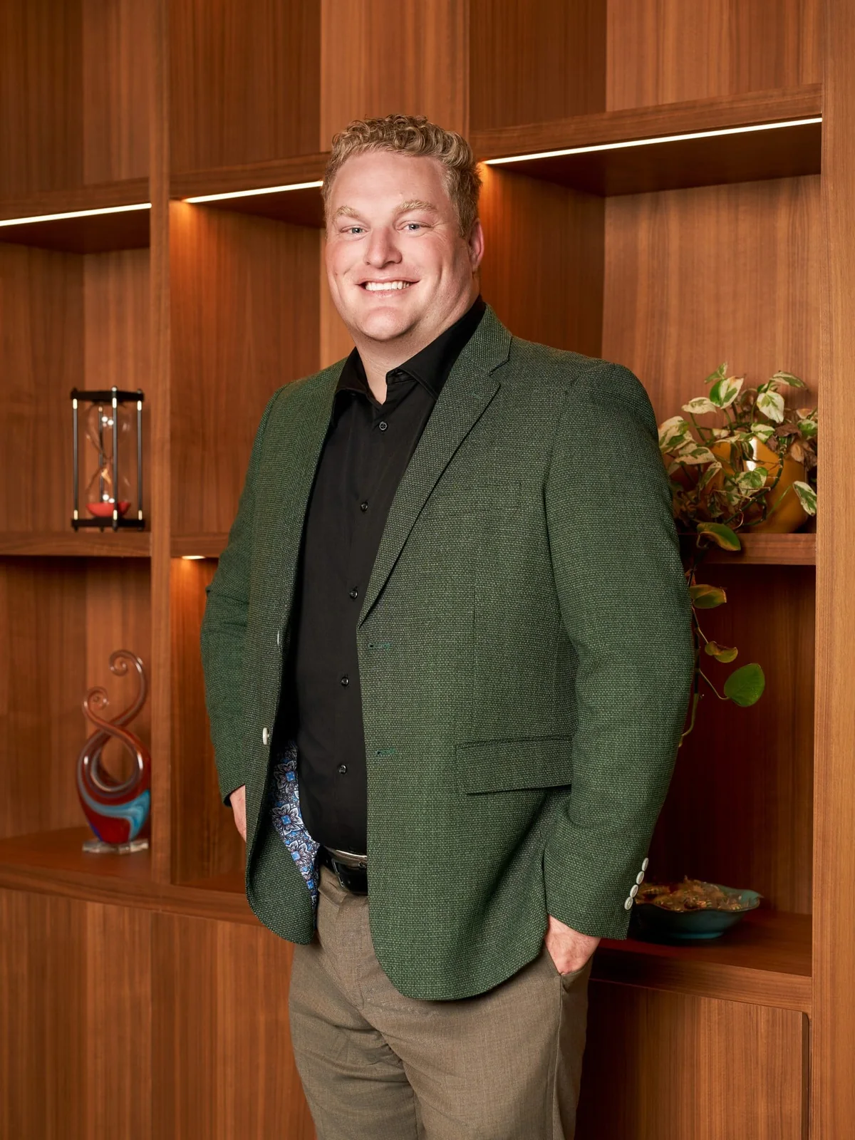 Portrait of a person in a green jacket standing in front of wood-paneled shelves.