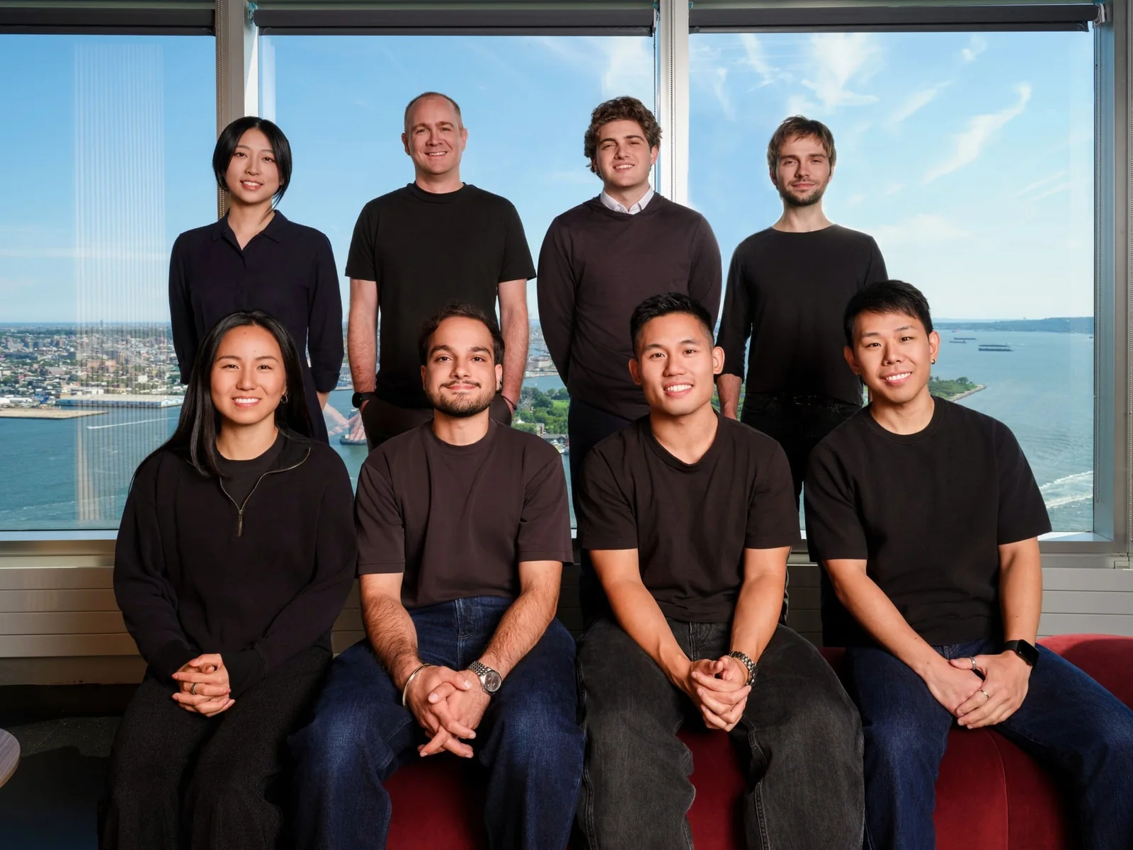 A group portrait of people arranged in two rows in front of large office windows.
