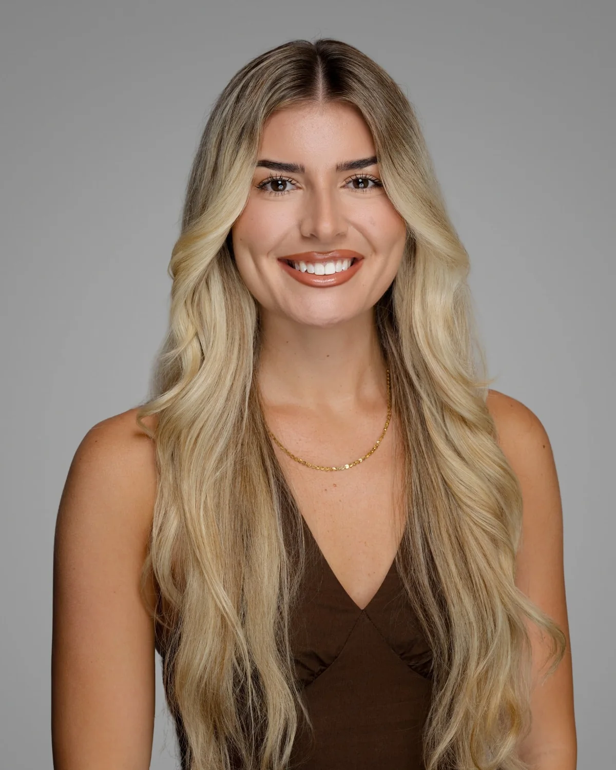 A person in a brown sleeveless top, centered against a gray backdrop.