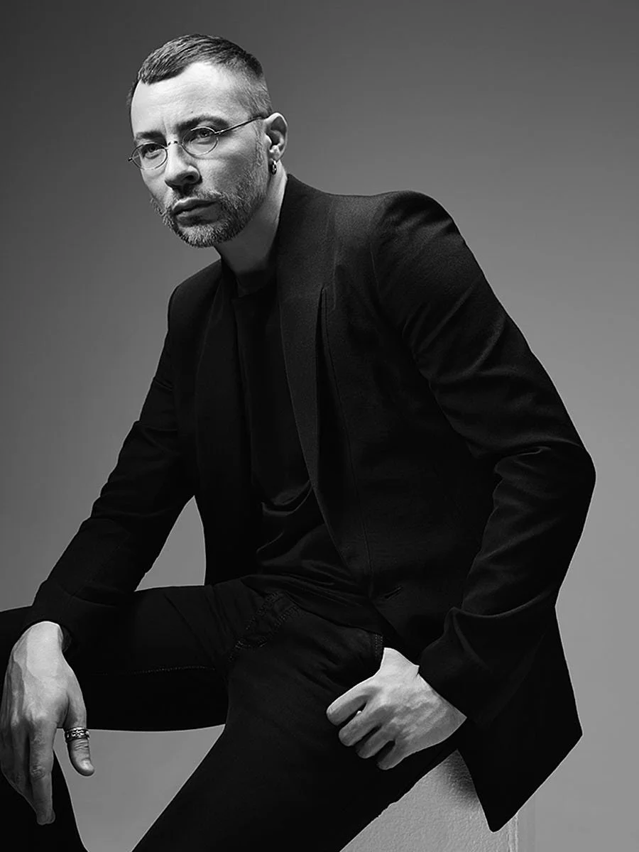 Black-and-white seated portrait of a man in glasses and a dark suit.
