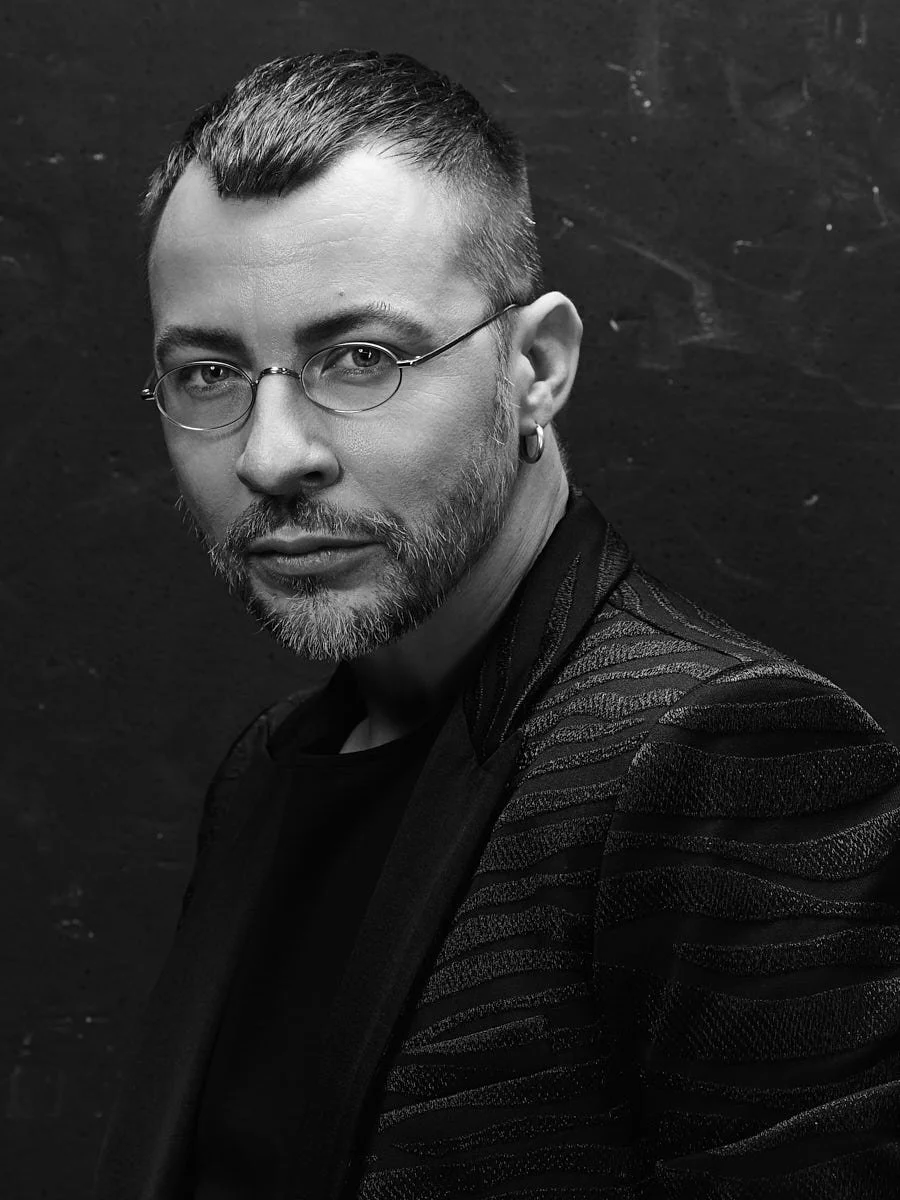 Black-and-white close portrait of a man in glasses and a dark jacket.