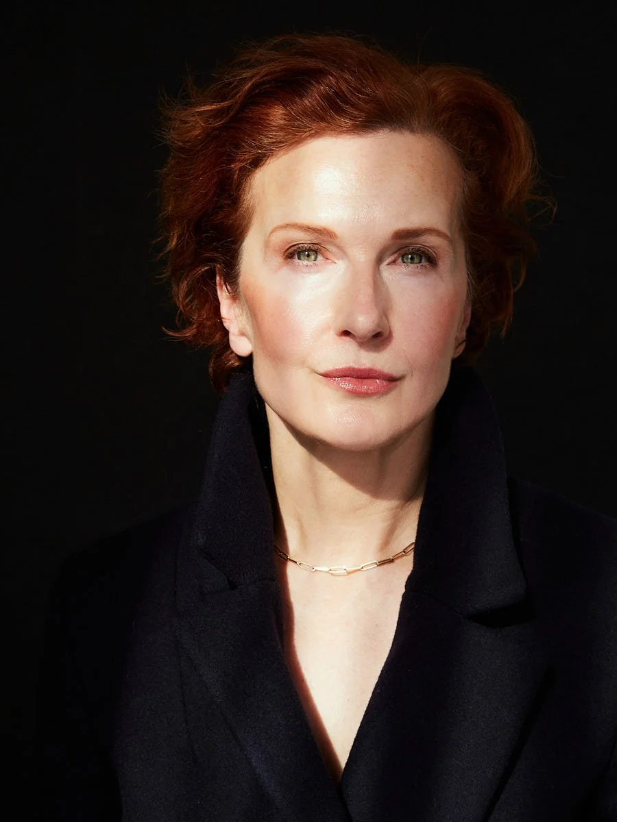 Close portrait of a red-haired woman in a dark blazer against black.