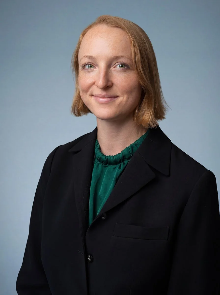 Person in a black blazer and green top against a blue background.