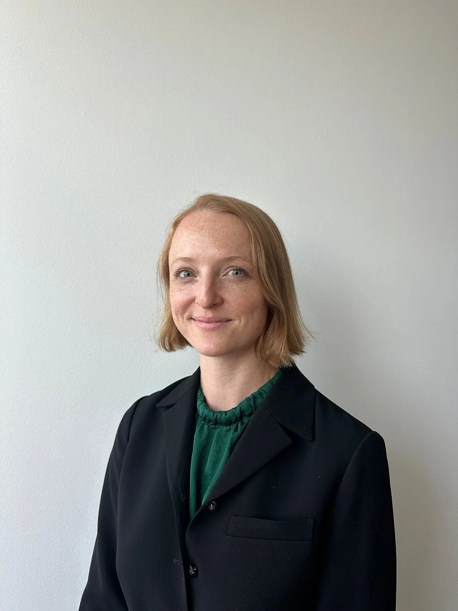 Person in a black blazer and green top against a light background.