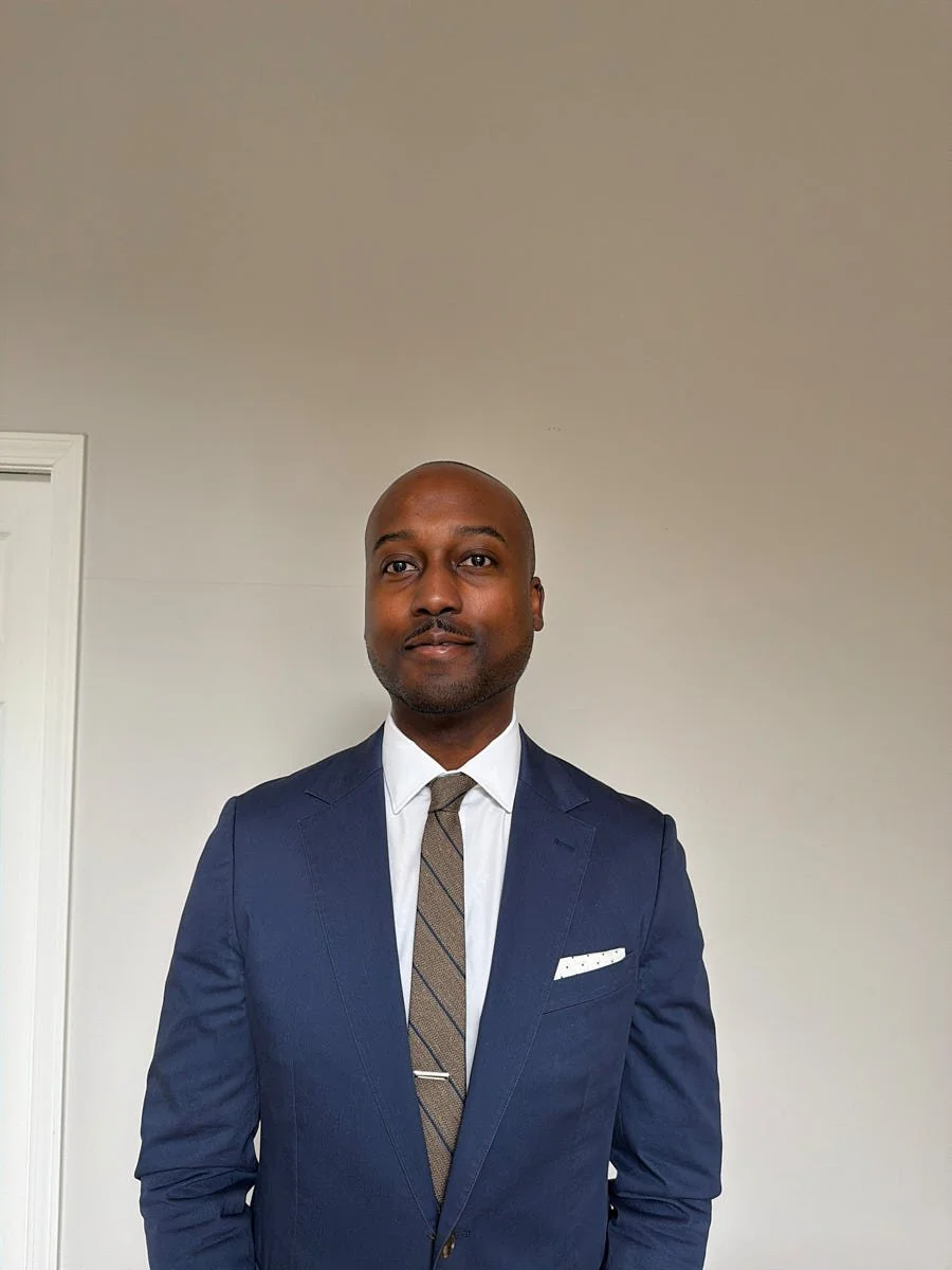 Person in a blue suit and tie standing against a light background.
