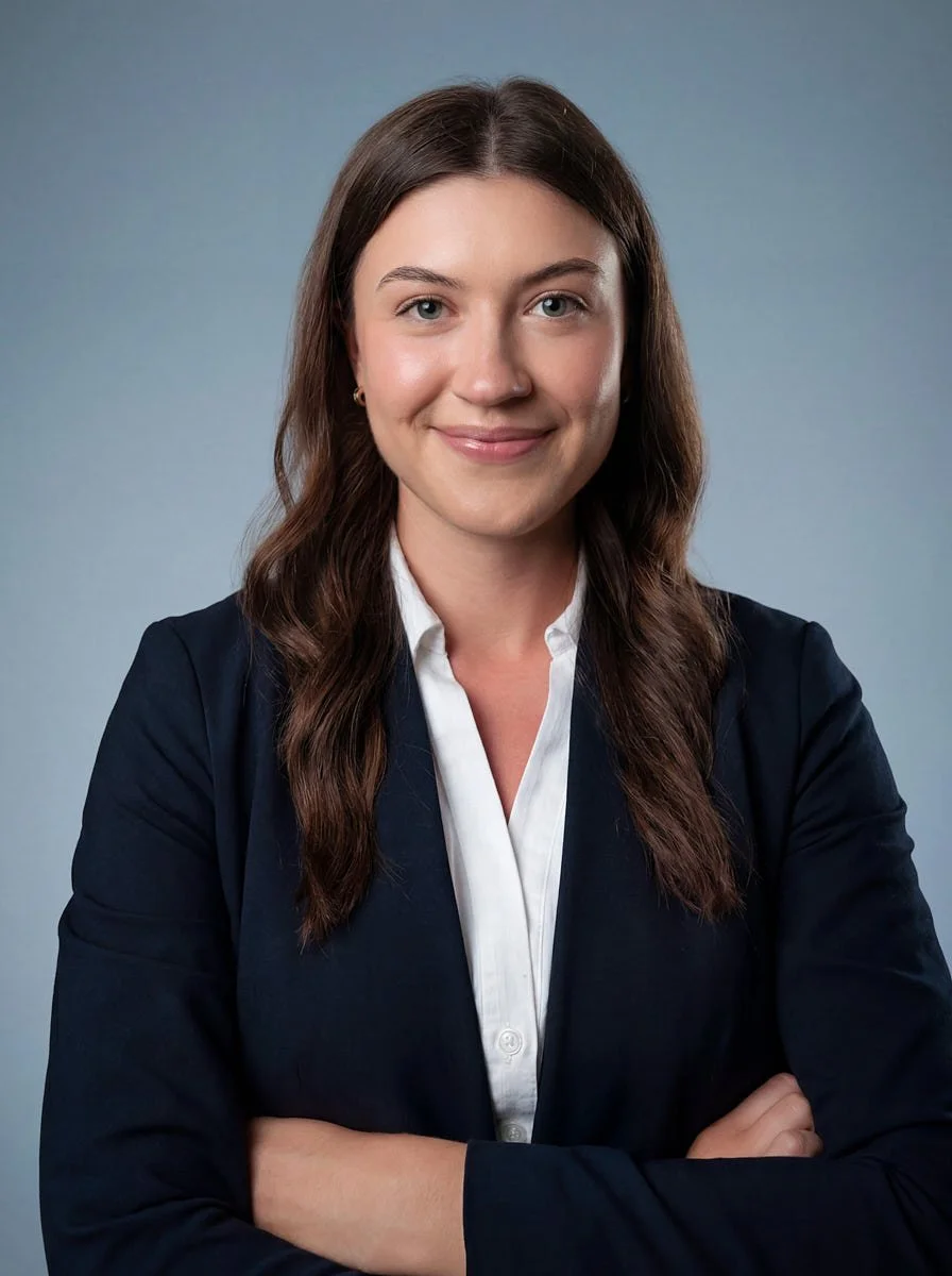 Person with long dark hair wearing a dark blazer and white top.