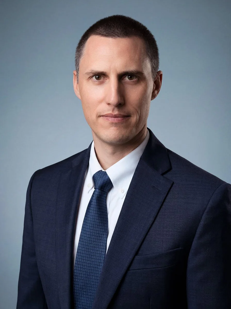 Person in a navy suit and blue tie against a light blue background.